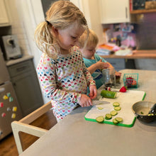 Load image into Gallery viewer, Two children in a kitchen, one cutting cucumbers on a cutting board.