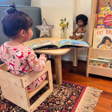 Load image into Gallery viewer, Child sitting on a wooden stool reading a book in a home setting with toys and books around.
