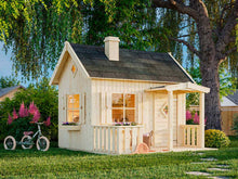 Load image into Gallery viewer, Exterior view of the completed DIY Playhouse Kit Little Cottage set in a garden, with a shingled roof, flower boxes, porch railing, and decorative windows by WholeWoodPlayhouses