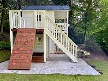 Load image into Gallery viewer, Side view of a luxury two-story wooden playhouse featuring a pink-handled climbing wall, slide, upper deck, and sandbox area below by WholeWoodPlayhouses