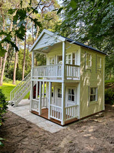 Load image into Gallery viewer, Charming two-story backyard playhouse with porch railings, a black roof, and multiple windows, set in a wooded area by WholeWoodCabins