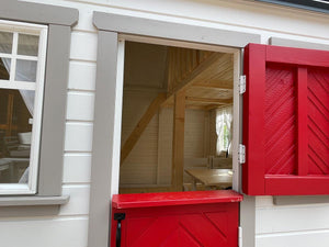Close- up of open red wooden Dutch door and view of interior with kids furniture and loft by WholeWoodPlayhouses