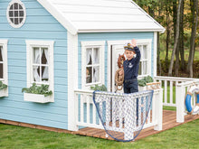 Load image into Gallery viewer, Boy waving on  Kids Outdoor Playhouse decorated wooden terrace with white railing by WholeWoodPlayhouses