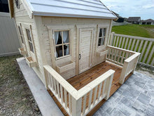Load image into Gallery viewer, Wooden playhouse with a natural finish, featuring a small porch, flower boxes beneath the windows, and a picket fence in the background. The playhouse is available for sale at Whole Wood Playhouses.