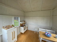 Load image into Gallery viewer, Interior view of the Peachtree 8x8 playhouse. White walls and natural wood play furniture. Natural wood floor. By WholeWoodPlayhouses