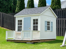 Load image into Gallery viewer, A view of the Peachtree 8x8 playhouse from the right. The playhouse has white walls, a dark roof, and vertically opening shed windows with a screen. The playhouse has a blue solid wood door that opens onto a terrace with white wood railings. The side windows have blue shutters. Made by WholeWoodPlayhouses.