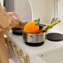 Load image into Gallery viewer, A child plays at cooking on the stove with a pot, surrounded by colorful vegetables.