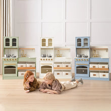 Load image into Gallery viewer, Two children are lying and playing on a wooden floor in front of colorful toy kitchen sets, with a wall with white panels behind them.
