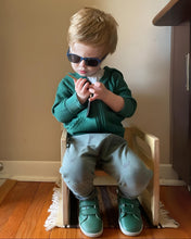 Load image into Gallery viewer, Child wearing sunglasses and a green sweater sitting on a wooden stool.
