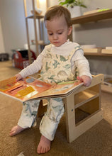 Load image into Gallery viewer, Child sitting on a wooden stool reading a colorful book indoors.