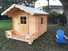 Load image into Gallery viewer, Front outside view of assembled wooden kids playhouse DIY Kit Little Cabin next to a blue chair | outdoor playhouse DIY kit by WholeWoodPlayhouses

