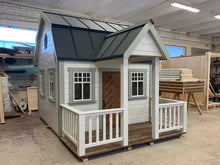 Load image into Gallery viewer, Outside of Kids Playhouse Grand Farmhouse Inside Of Workshop With Black Metal Roof And White Outdoor Siding And Gray Trims, Brown Fishbone Wooden Door, Terrace And White Railings by WholeWoodPlayhouses