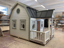 Load image into Gallery viewer, Outside of Kids Playhouse Grand Farmhouse Inside Of Workshop With Black Metal Roof And White Outdoor Siding And Gray Trims, Brown Fishbone Wooden Door, Terrace And White Railings And Round Top Window by WholeWoodPlayhouses