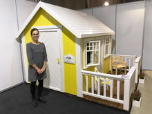 Load image into Gallery viewer, Woman standing in front of yellow Kids Playhouse Sunshine with a white roof by WholeWoodPlayhouses