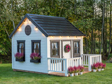 Load image into Gallery viewer, Wooden Playhouse Blacbird with a round top window, black flower boxes with pink flowers and black roof decorated with flights by WholeWoodPlayhouses