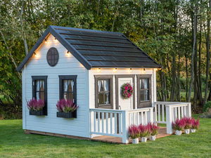 Wooden Playhouse Blacbird with a round top window, black flower boxes with pink flowers and black roof decorated with flights by WholeWoodPlayhouses