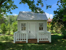 Load image into Gallery viewer, Front view of Kids Playhouse Snowy Owl with black trims, wooden terrace with white railing and flower boxes in the garden by WholeWoodPlayhouses