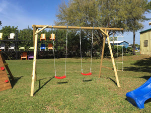 Outdoors kids swingset Magnus by WholeWoodPlayhouses with two swings and a rope ladder on a sunny day on green grass