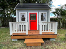 Load image into Gallery viewer, Wooden Playhouse  Boy Cave with black roof, red glass door and a wooden terrace with white railing in a backyard by WholeWoodPlayhouses
