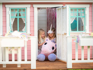 Two kids playing with Pink fluffy Unicorn in a pink wooden playhouse with a wooden terrace with white railings by WholeWoodPlayhouses