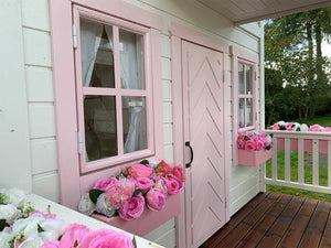 2- story Custom Wooden Playhouse Closeup of front windows and pink flower boxes with pink flowers and fishbone door by WholeWoodPlayhouses
