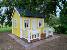 Load image into Gallery viewer, Wooden Playhouse in yellow color  witw black metal roof and wooden terrace with white railing in the backyard by WholeWoodPlayhouses