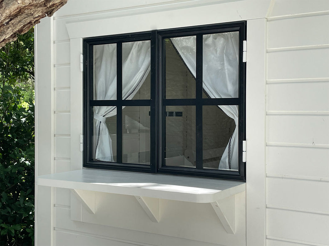Black-framed playhouse window with white curtains and built-in serving shelf for shop-style play.