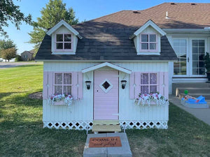 Wooden Farmhouse Style Kids Outdoor Playhouse DIY Kit Little Farmhouse With white Walls, pink flower boxes and brown roof with small windows in the Backyard by WholeWoodPlayhouses