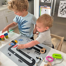 Load image into Gallery viewer, Two children playing with toys on a road mat in a kitchen.

