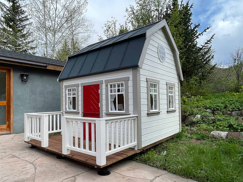  Outdoor Playhouse Farmhouse with black metal roof, a round top window and wooden terrace white wooden railing in the backyard by WholeWoodPlayhouses