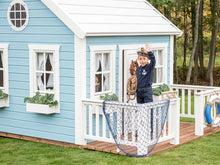 Load image into Gallery viewer, Boy waving on  Kids Outdoor Playhouse decorated wooden terrace with white railing by WholeWoodPlayhouses
