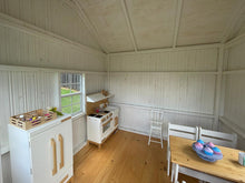 Load image into Gallery viewer, Interior view of the Peachtree 8x8 playhouse. White walls and natural wood play furniture. Natural wood floor. By WholeWoodPlayhouses
