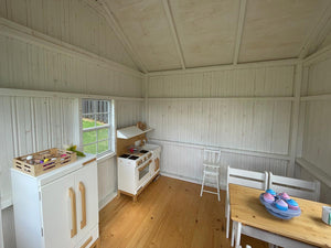 Interior view of the Peachtree 8x8 playhouse. White walls and natural wood play furniture. Natural wood floor. By WholeWoodPlayhouses