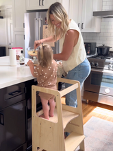 Load image into Gallery viewer, Woman and child in a kitchen with the woman helping the child on a step stool.
