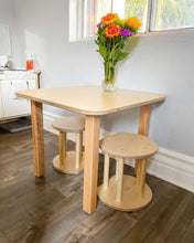 Load image into Gallery viewer, Wooden play dining table with three stools in a room with a window and kitchen area.
