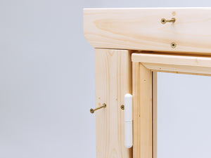 Close-up of wooden playhouse window frame with white hinge and visible installation screws