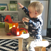Load image into Gallery viewer, Child playing with colorful wooden blocks on a table in a room with books and a rug.
