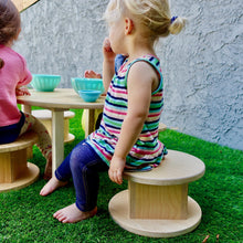 Load image into Gallery viewer, Children sitting on wooden stools around a small table outdoors.
