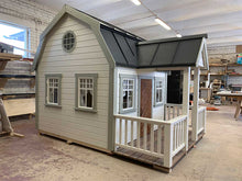 Load image into Gallery viewer, Outside of Kids Playhouse Grand Farmhouse Inside Of Workshop With Black Metal Roof And White Outdoor Siding And Gray Trims, Brown Fishbone Wooden Door, Terrace And White Railings And Round Top Window by WholeWoodPlayhouses
