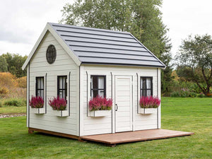 Outdoor Playhouse in black and white color with wooden terrace, a round top window and flower boxes with pink flowers in the backyard by WholeWoodPlayhouses