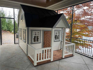 White and light gray Kids Playhouse Grand Farmhouse with Brown Fishbone Style Wooden Door, a Terrace And White Railings on the porch by WholeWoodPlayhouses