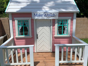 Closeup of front side of Pink Outdoor Playhouse Unicorn with  metal roof, two opening windows, white door, wooden terrace with white railing by WholeWoodPlayhouses