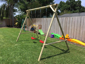 Side view of kids swing set Mathias with two swings by WholeWoodPlayhouses on a sunny day on green grass