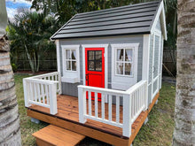 Load image into Gallery viewer, Wooden Playhouse Boy Cave With Black Metal Roof, a terrace with white railing and Red Half Glass Door in the backyard By WholeWoodPlayhouses
