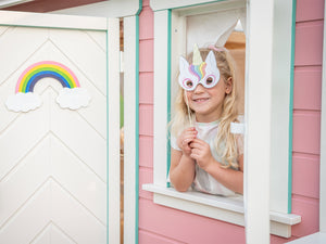 A girl with Unicorn mask looking out of a pink wooden playhouse window by WholeWoodPlayhouses
