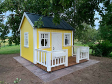 Load image into Gallery viewer, Wooden Playhouse in yellow color  witw black metal roof and wooden terrace with white railing in the backyard by WholeWoodPlayhouses

